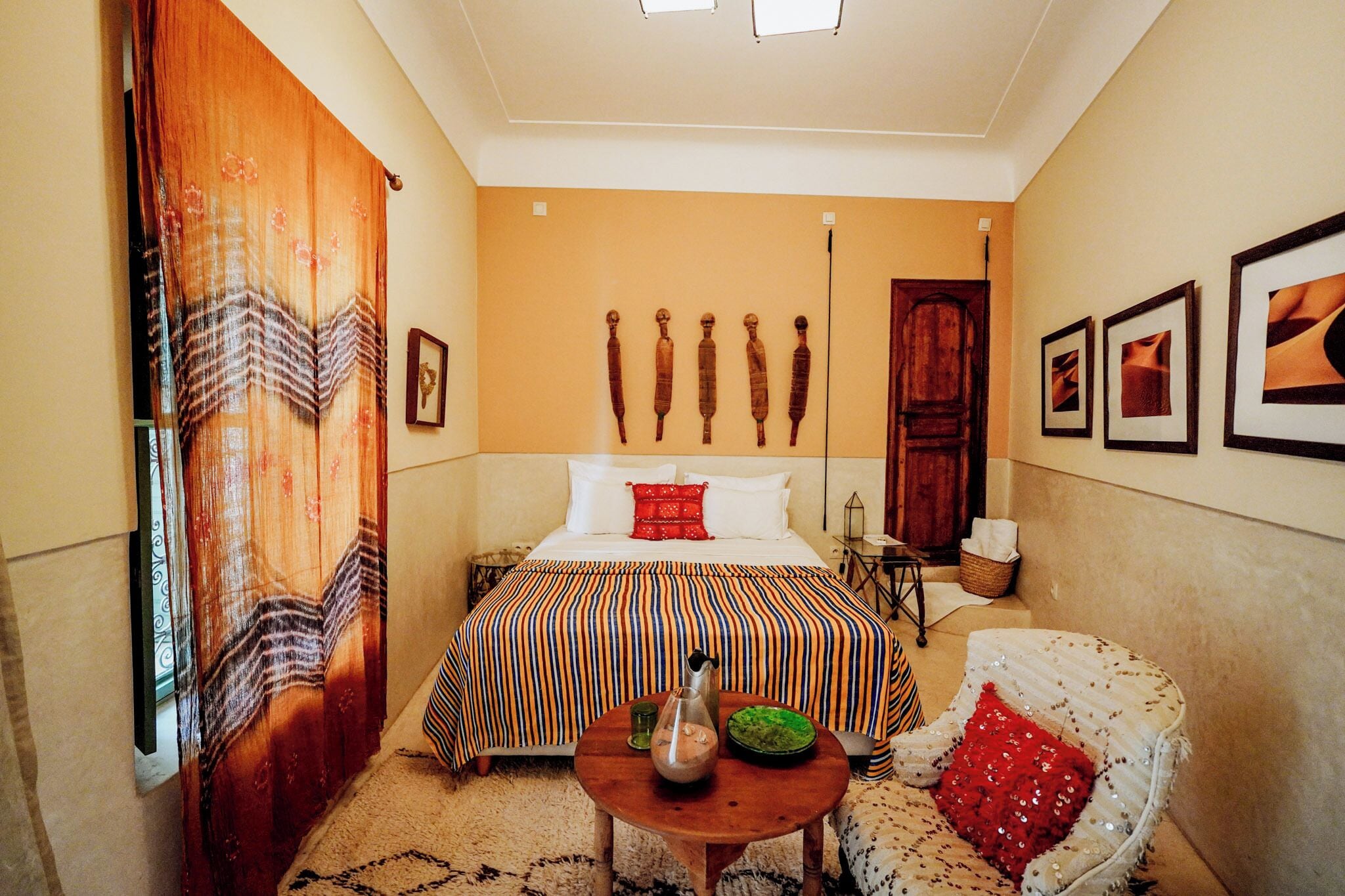 A hotel room with a bed, a chair, a small table, and a wall with framed pictures.