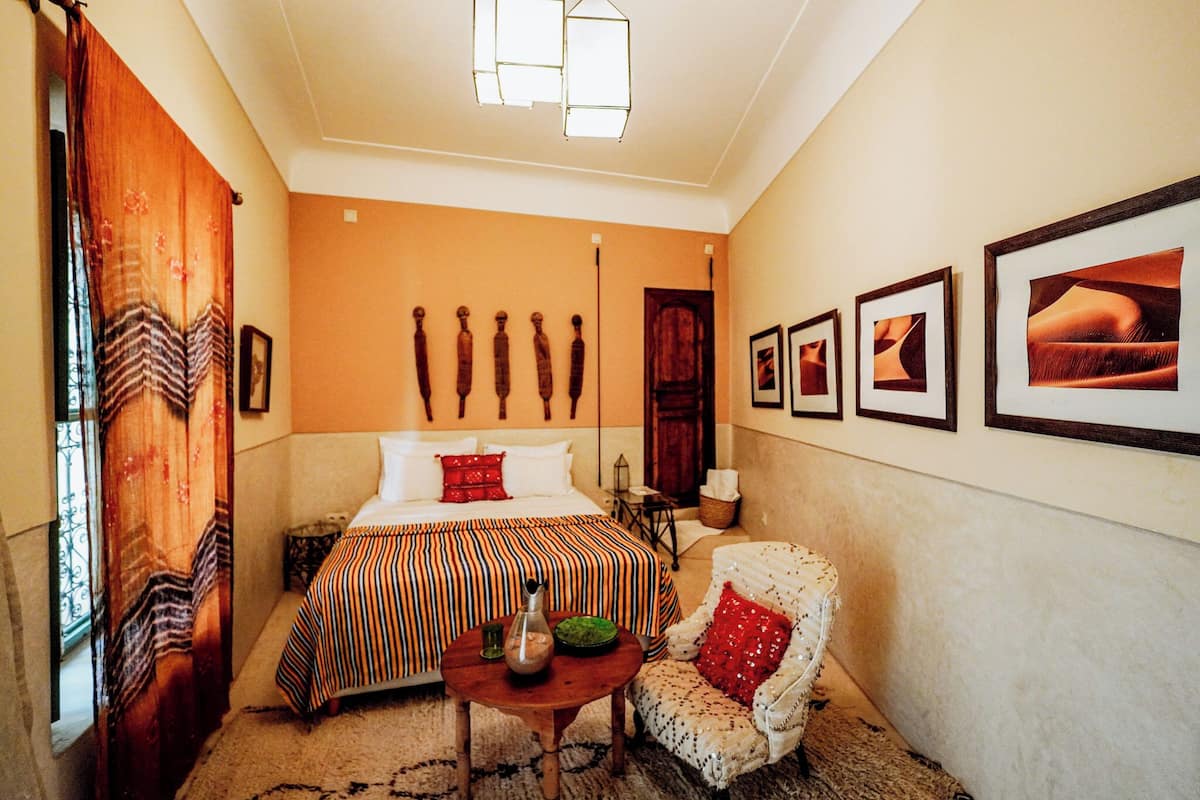 A hotel room with a bed, a chair, a table, and wall-mounted artwork.