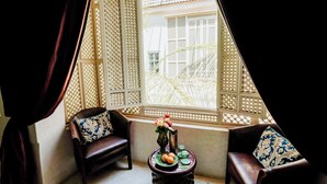 Une pièce avec une fenêtre à treillis offrant une vue agréable, deux fauteuils en cuir et une petite table sur laquelle se trouvent un vase et des fruits.