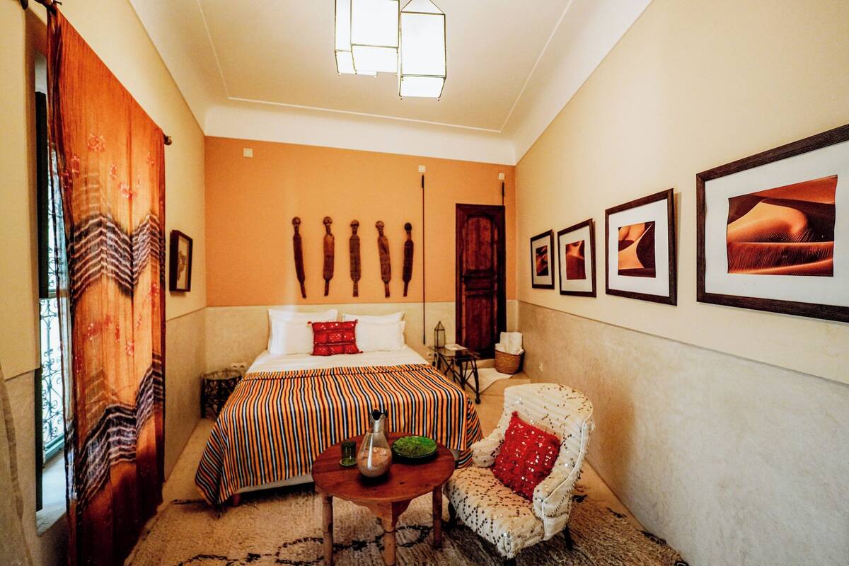 A hotel room with a bed, a chair, a table, and wall-mounted artwork.