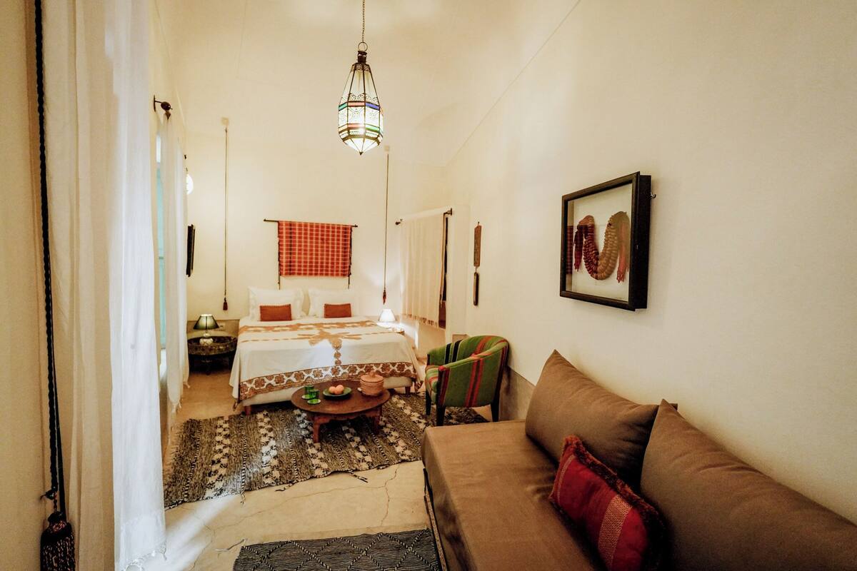 A cozy room with a bed, a sofa, a small table with fruit, and a hanging light fixture.