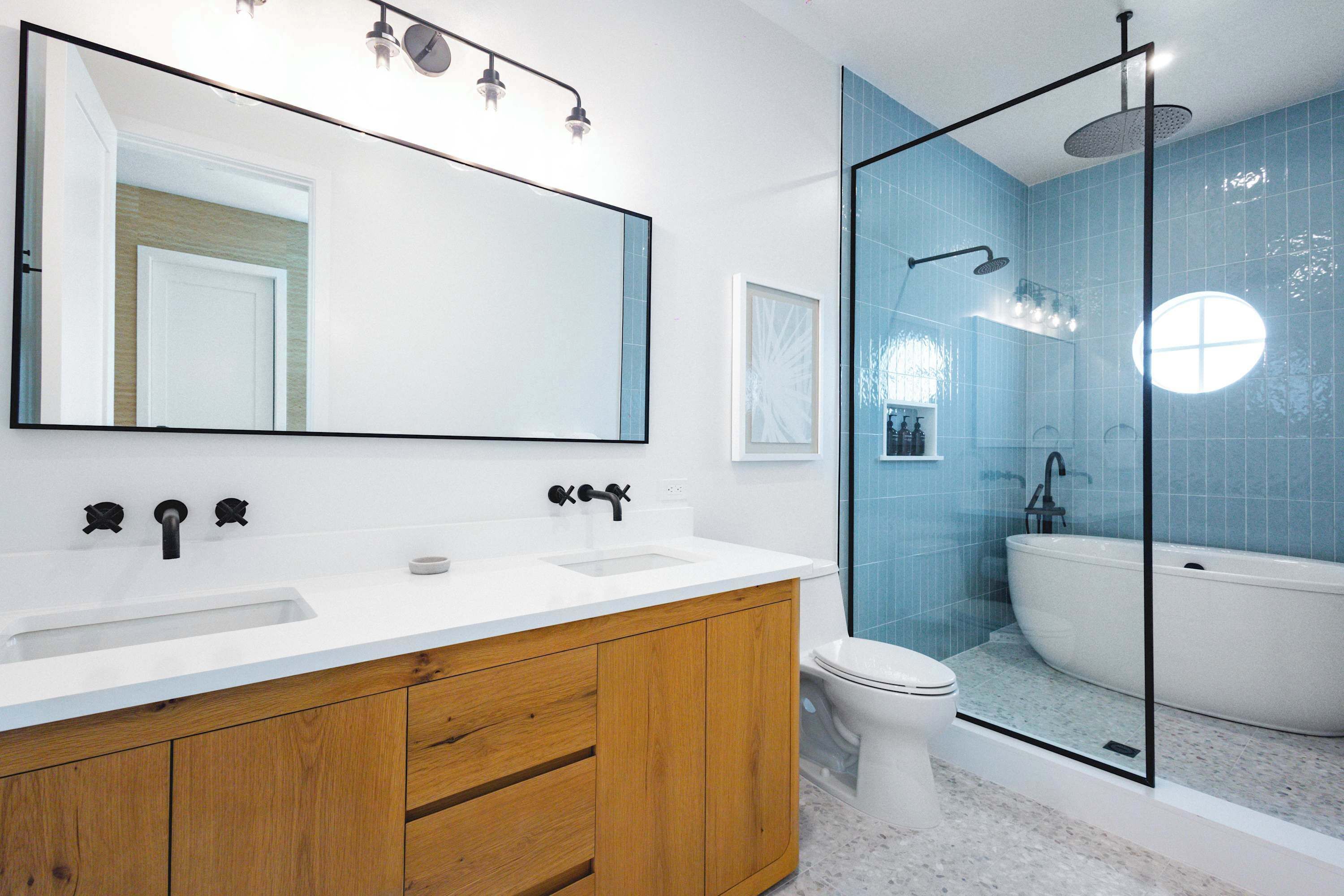 Une salle de bain moderne avec un grand miroir, deux lavabos, des toilettes et une douche séparée par une paroi en verre.