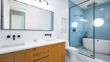 Une salle de bain moderne avec un grand miroir, deux lavabos, des toilettes et une douche séparée par une paroi en verre.