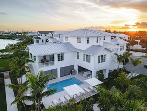A large white house with a pool, surrounded by palm trees and a view of the sunset.