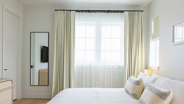 Un dormitorio con una cama grande, un espejo, una ventana con cortinas y una mesita de noche.
