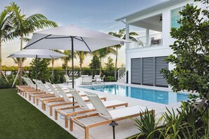 A poolside area with sun loungers and umbrellas, a pool, and a two-story building with a balcony. - The Joyrise House at Solaire Lunara Bay (Key West)
