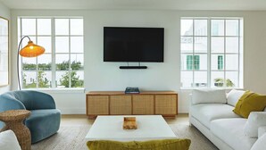 En stue med stort vindue, fladskærms-tv, sofa, sofabord og en lampe.