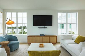 A living room with a large window, a flat-screen TV, a sofa, a coffee table, and a lamp. - The Joyrise House at Solaire Lunara Bay (Key West)