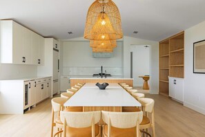 A modern kitchen with white cabinetry, a central island, and a dining area with a long table and chairs.
