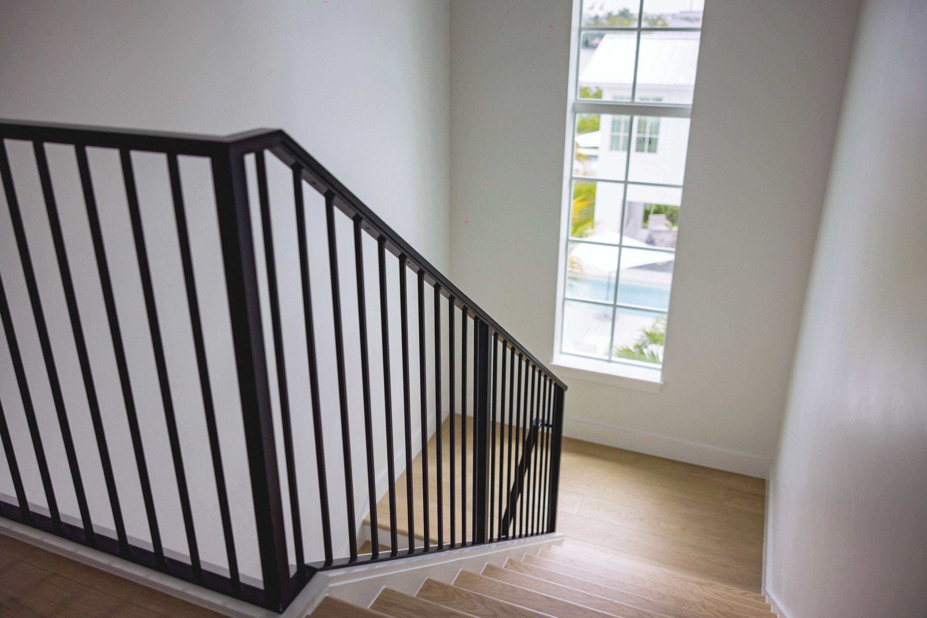 Una escalera con barandilla negra y escalones de madera que conduce a una habitación con un ventanal grande.