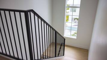 Una escalera con barandilla negra y escalones de madera que conduce a una habitación con un ventanal grande.
