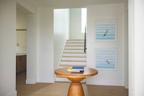 Un pasillo con una escalera de madera, una mesa redonda de madera con libros y dos cuadros en la pared.