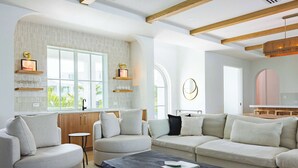 A modern living room with a sectional sofa, a coffee table, and a kitchen area with a window. - The Fairhaven House at Solaire Lunara Bay (Key West)