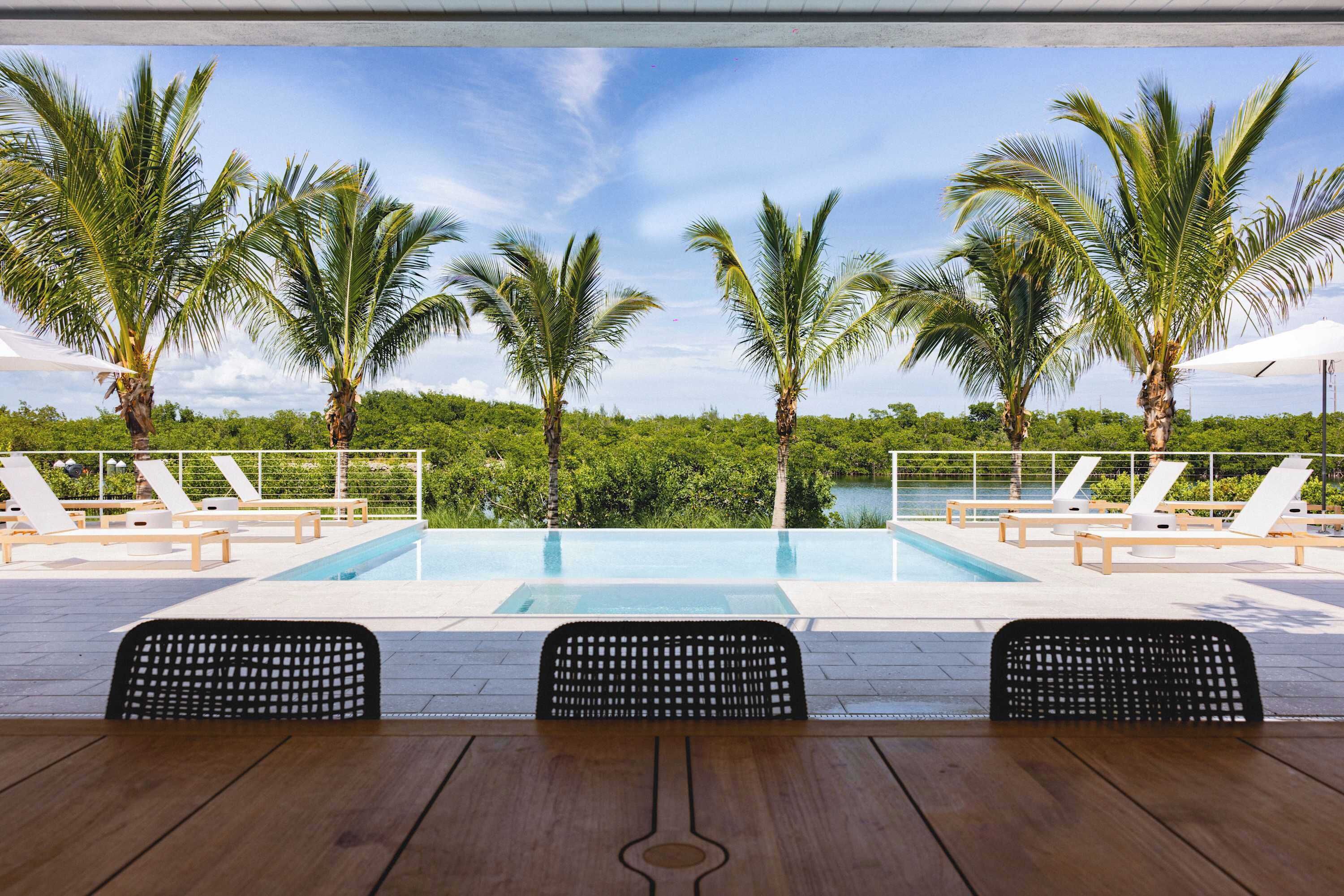 A poolside area with lounge chairs, a wooden table, and palm trees.