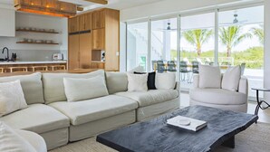 A modern living room with a sectional sofa, a coffee table, and a dining area with outdoor seating. - The Fairhaven House at Solaire Lunara Bay (Key West)