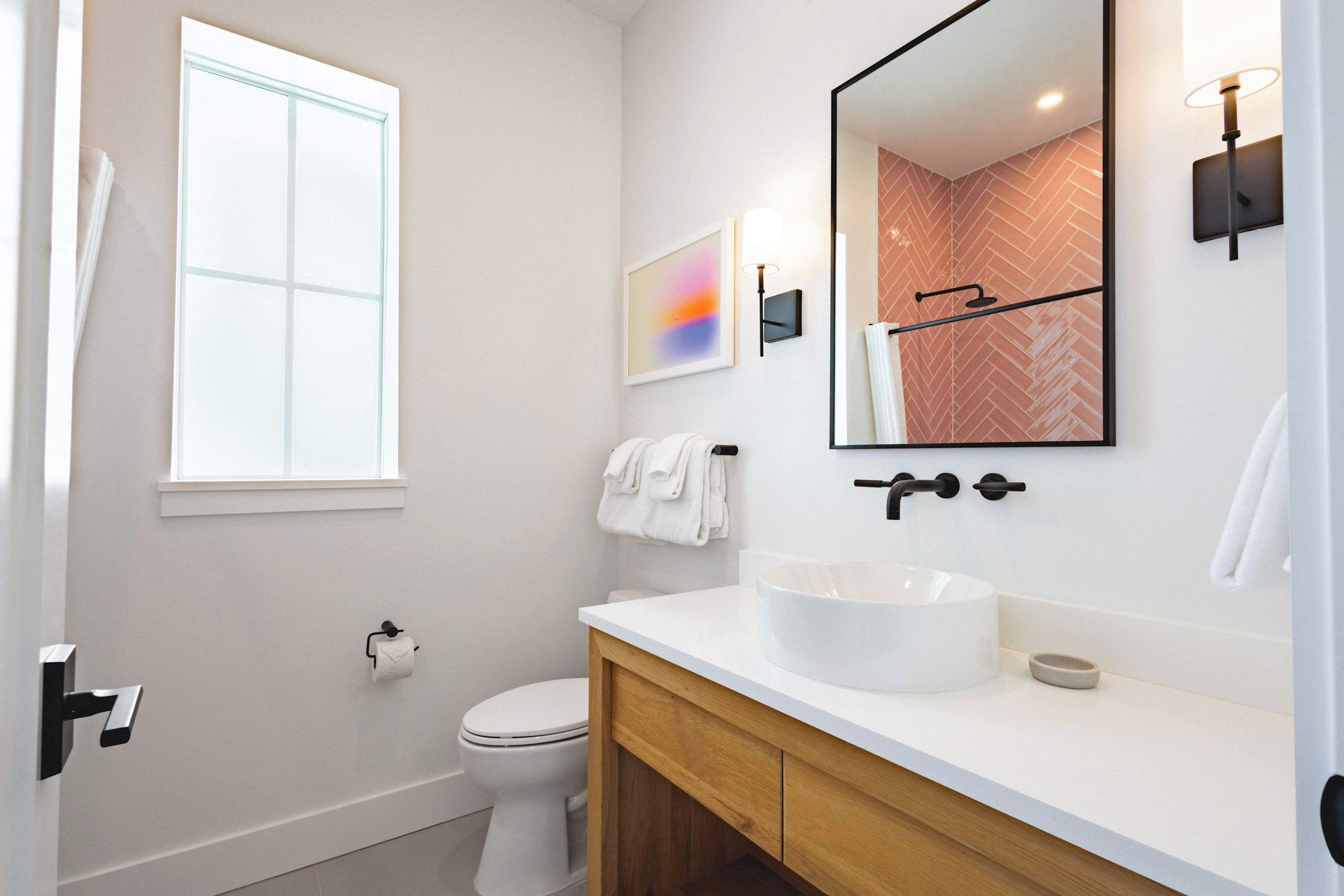 A modern bathroom with a white sink, wooden vanity, a large mirror, and a herringbone-patterned shower wall.