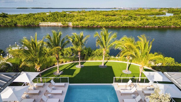 A pool area with lounge chairs and palm trees, overlooking a body of water and greenery. - The Fairhaven House at Solaire Lunara Bay (Key West)