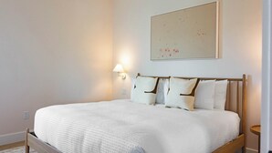 A neatly made bed with a white duvet, a wooden headboard, and a wall-mounted light fixture. - The Fairhaven House at Solaire Lunara Bay (Key West)