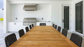 Eine moderne Außenküche mit Holztisch und -stühlen, einem Gasherd und einem Deckenventilator.