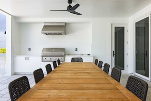 Eine moderne Außenküche mit Holztisch und -stühlen, einem Gasherd und einem Deckenventilator.