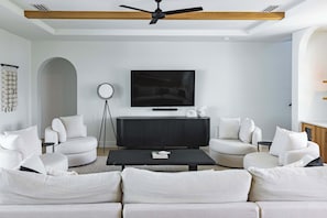Ein modernes Wohnzimmer mit einer schwarzen Unterhaltungsecke, weißen Sofas und einem Deckenventilator.