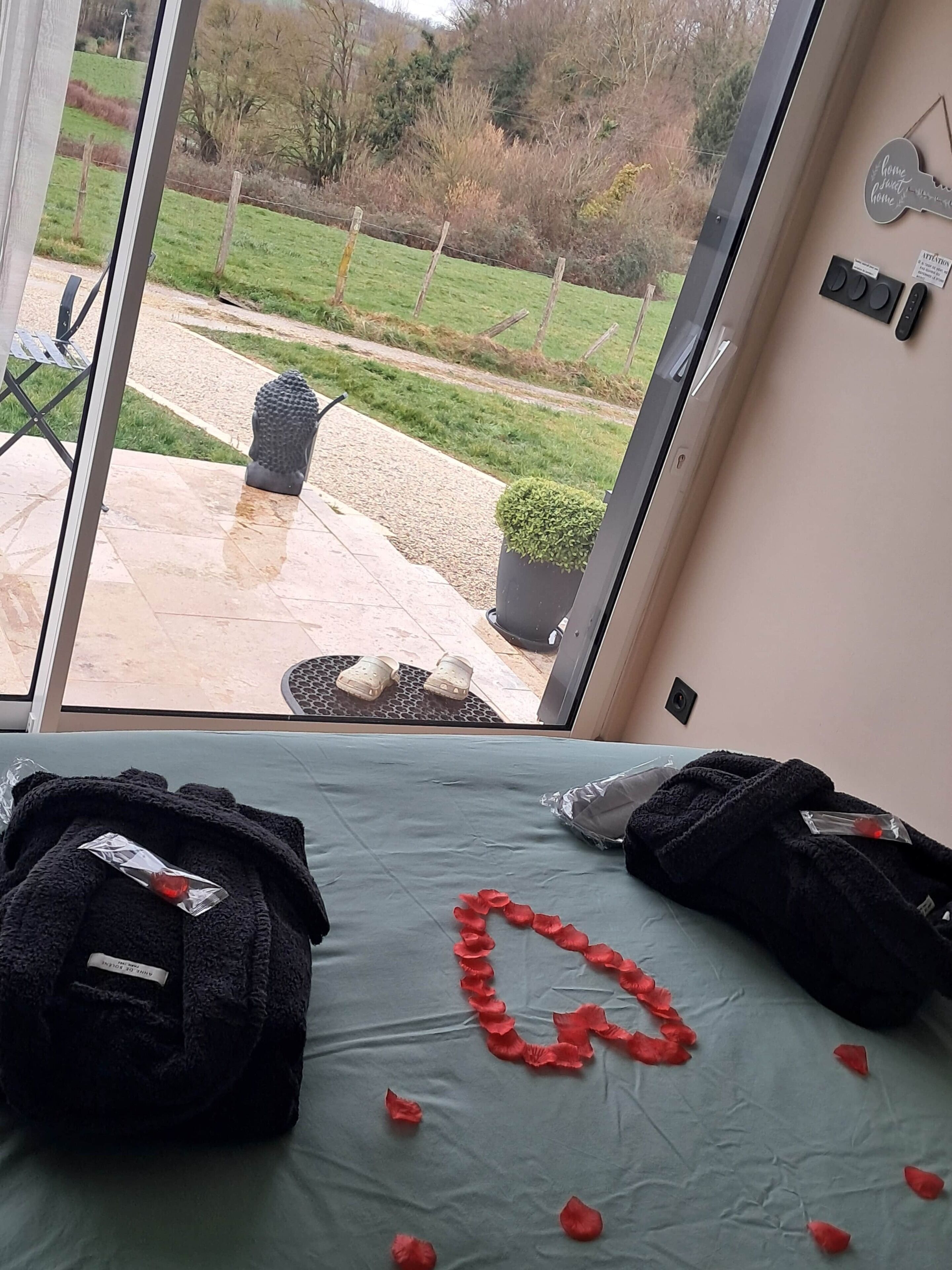 A room with a bed, a view of a garden through a glass door, a small table with a chair, and a wall with a key-shaped decoration.