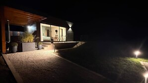 Una casa moderna amb un porxo cobert, un dormitori visible i un camí que condueix a l'entrada.