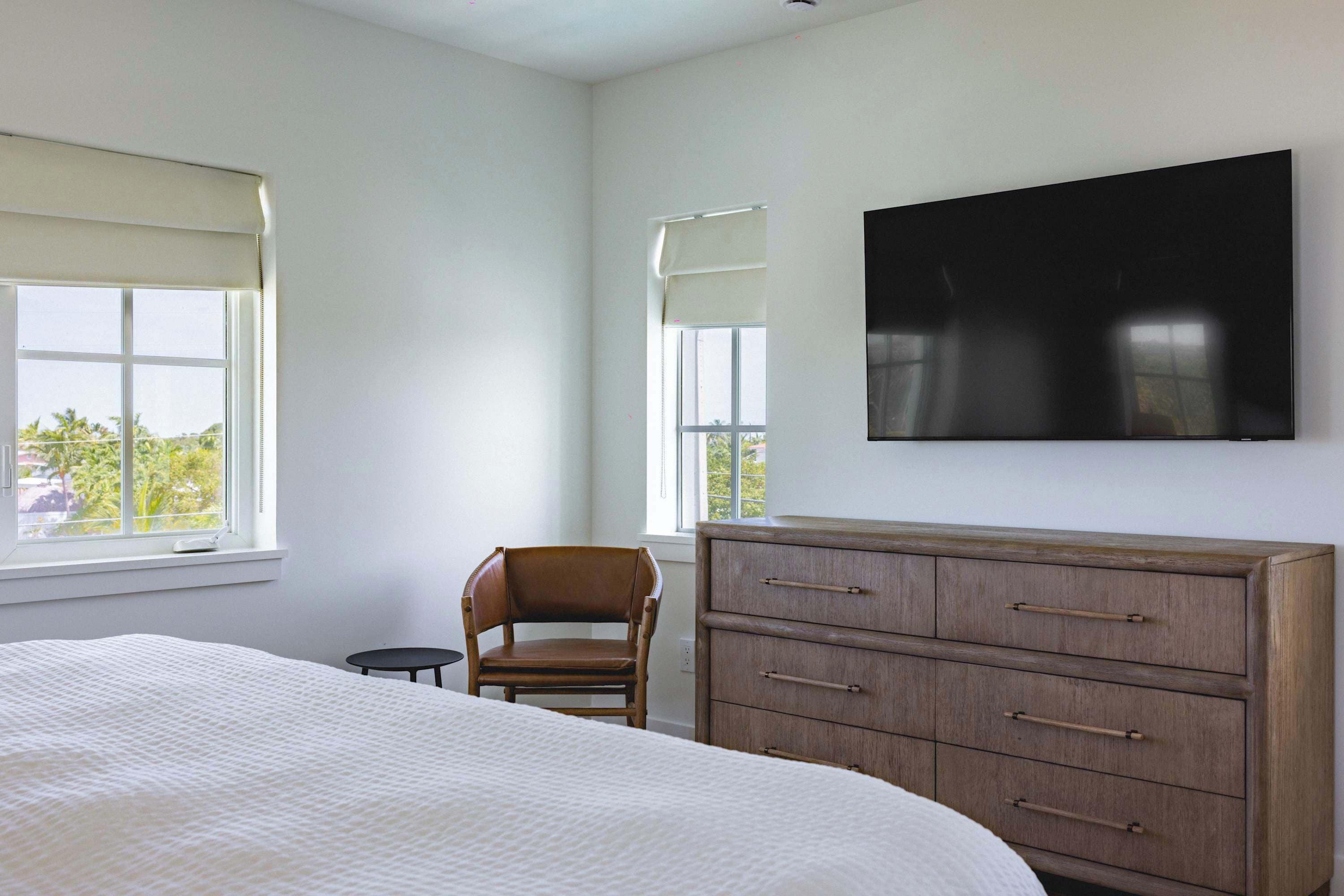 Een slaapkamer met een groot bed, een houten dressoir, een stoel en een flatscreen televisie aan de muur.