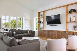 Een moderne woonkamer met een grote flatscreen-televisie, grijze banken, een witte salontafel en een houten boekenkast.