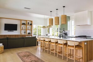 Une cuisine moderne dotée d’un îlot central, de tabourets de bar, de luminaires suspendus et d’un téléviseur encastré.