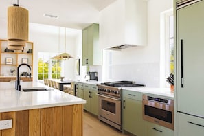 Een moderne keuken met een centraal eiland, roestvrijstalen apparatuur en een groot raam voor natuurlijk licht.
