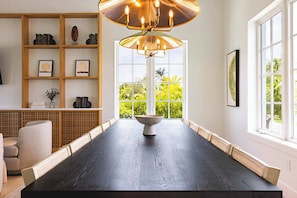 Een moderne eetruimte met een donker houten tafel, een centraal geplaatste schaal en een boekenkast met boeken en decoratieve objecten.