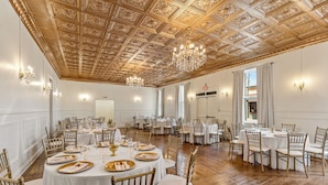 Ein Bankettsaal mit runden Tischen, goldenen Stühlen und Kronleuchtern.