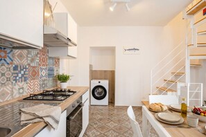 A compact kitchen with a washing machine, a dining area with a table set for two, and a staircase with a white railing. - Gabbiano 7 - Cozy Ground-Floor Apartment  (Bari)