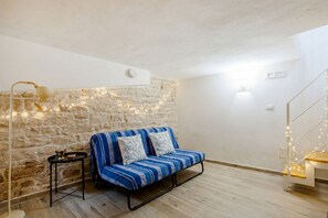 A room with a stone wall, a blue-striped sofa, a small table, and a staircase with lights.