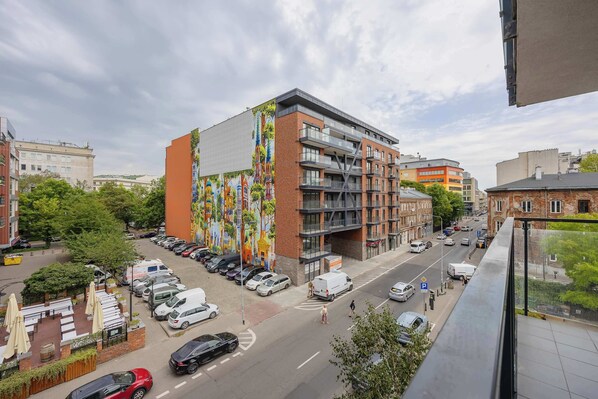 Un edificio de varios pisos con un mural colorido en la fachada, un estacionamiento con varios coches y una vista de la calle con edificios y vegetación.