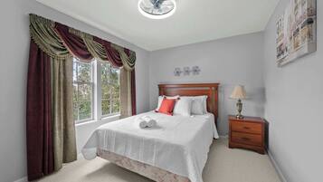 A bedroom with a bed, a nightstand with a lamp, a window with curtains, and a ceiling fan.