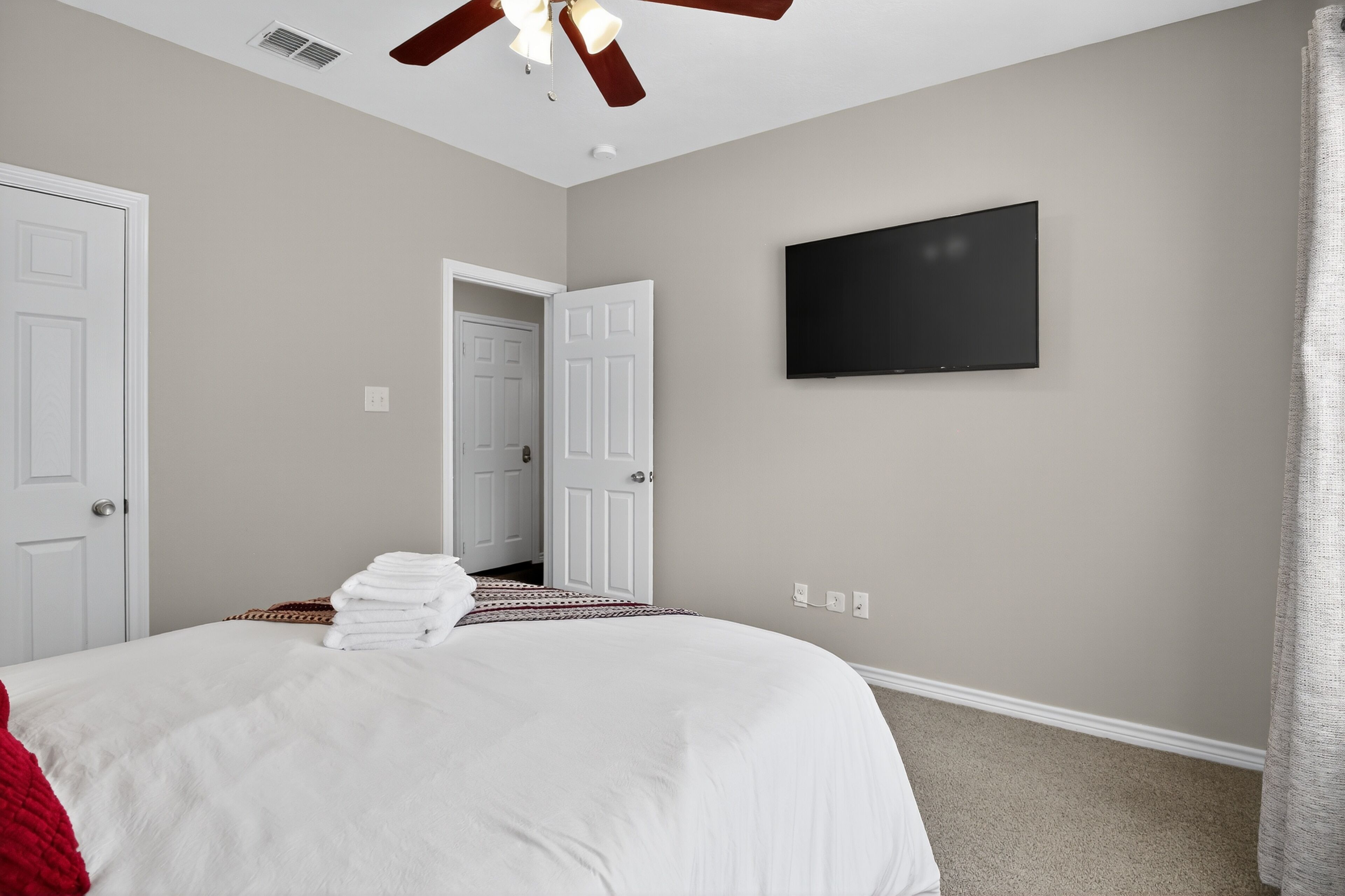Une chambre dotée d’un grand lit, d’un ventilateur de plafond, d’un téléviseur à écran plat et d’une porte donnant sur une autre pièce.