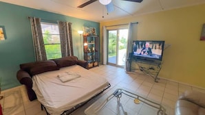 Un dormitorio con cama, televisión, mesita de noche y ventana con cortinas.