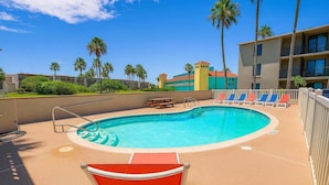 Una piscina con sillas de descanso y una mesa, rodeada de palmeras y edificios.