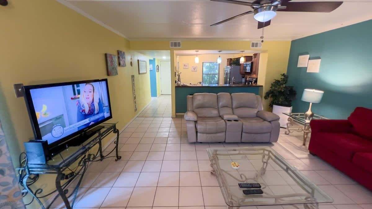 A living room with a flat-screen TV, a sofa, a red couch, and a glass coffee table.
