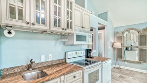 Una cocina con gabinetes blancos, encimera de granito, pileta de acero inoxidable, microondas, estufa y lavavajillas.