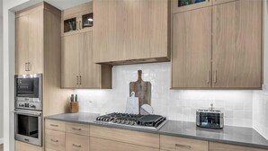 A modern kitchen with light wood cabinets, stainless steel appliances, and a marble backsplash.
