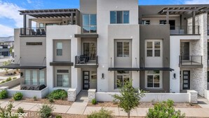 A modern multi-story apartment building with balconies, large windows, and a landscaped front yard.