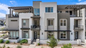 A modern multi-story apartment building with balconies, large windows, and a landscaped front yard.