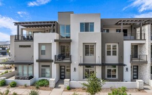 A modern multi-story apartment building with balconies, large windows, and a landscaped front yard.