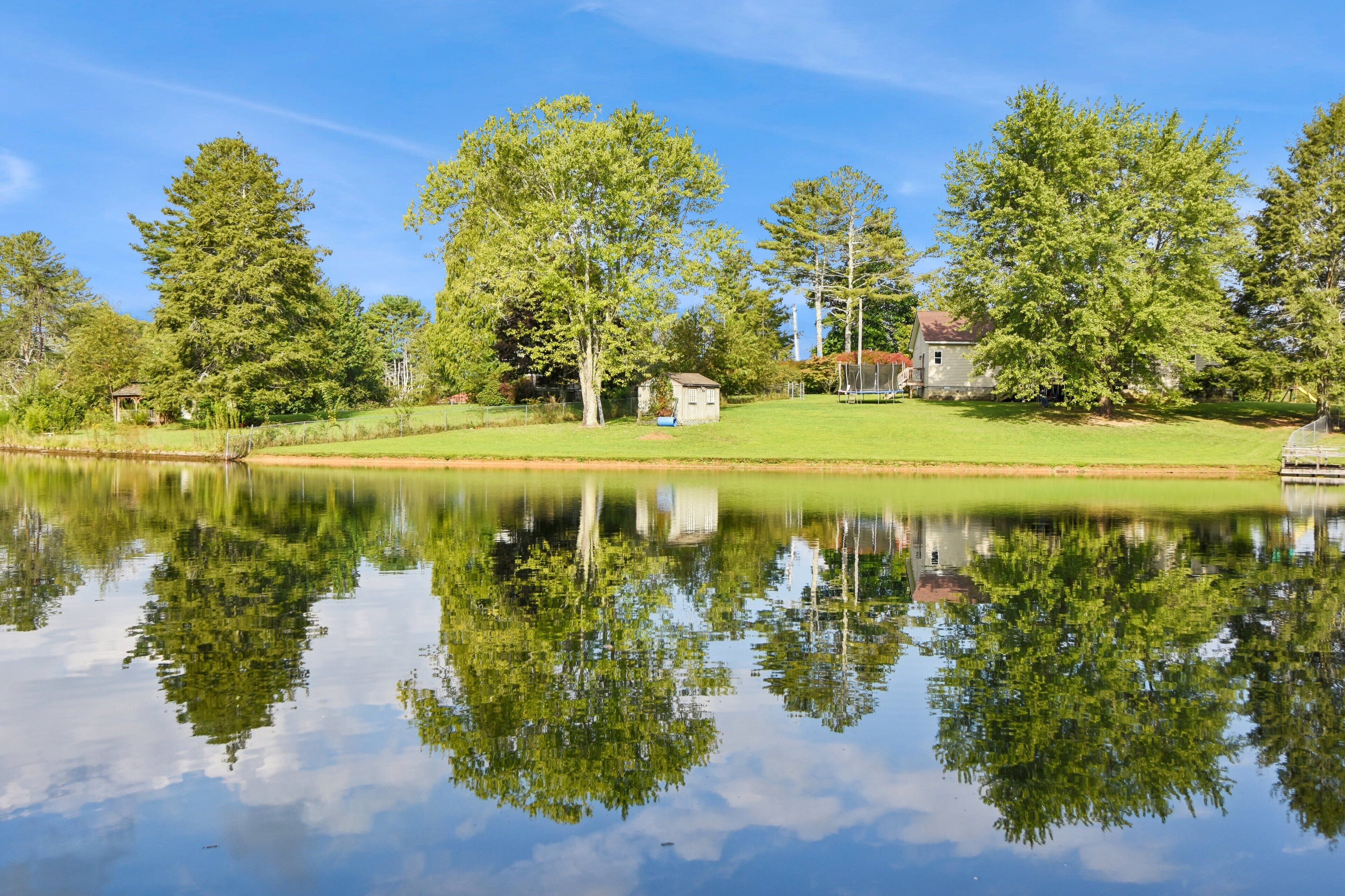 A serene lakeside scene with a house, trees, and a clear reflection on the water.