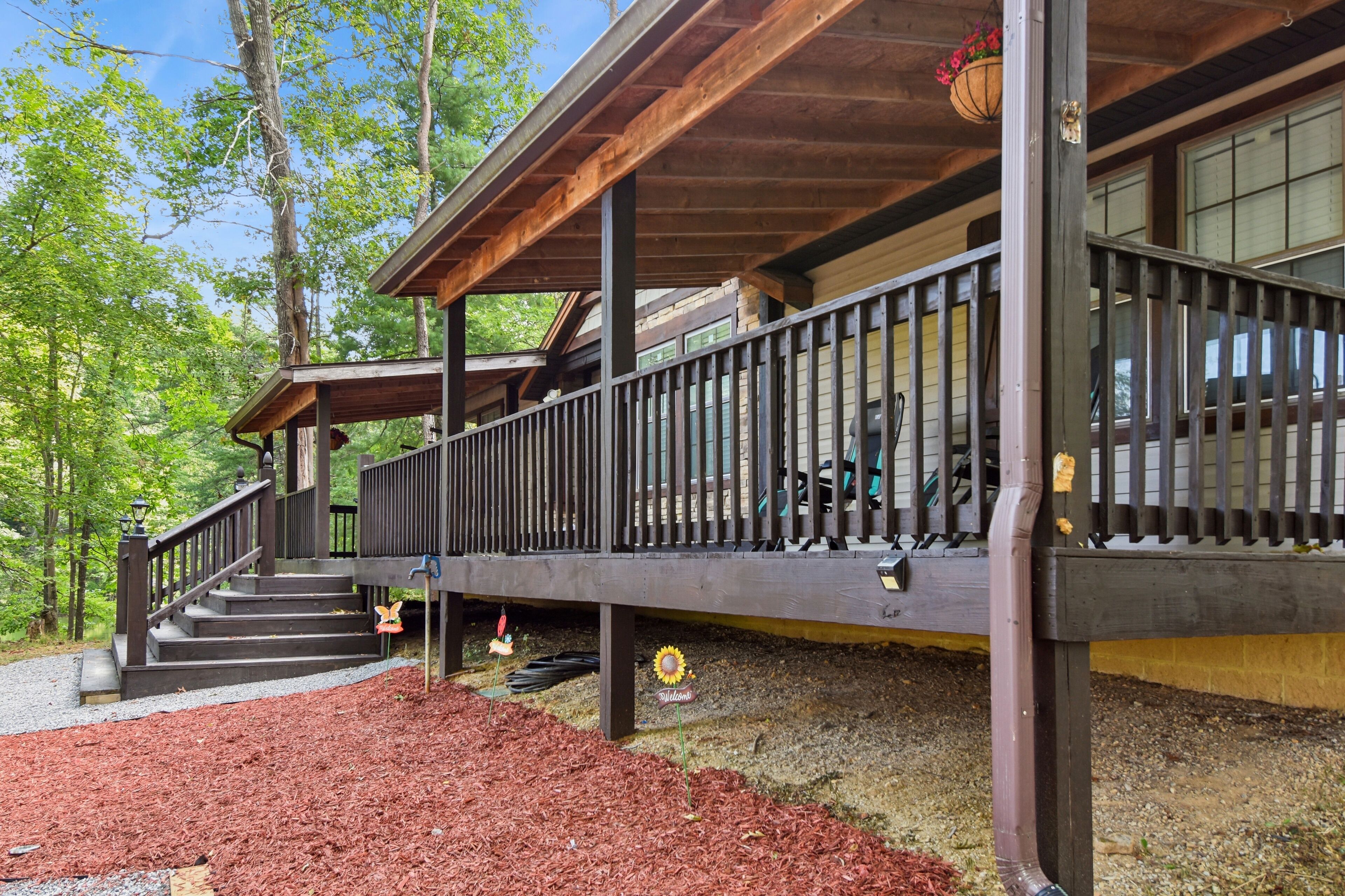 A wooden deck with a railing, steps leading up to a covered area, and a hanging flower basket.
