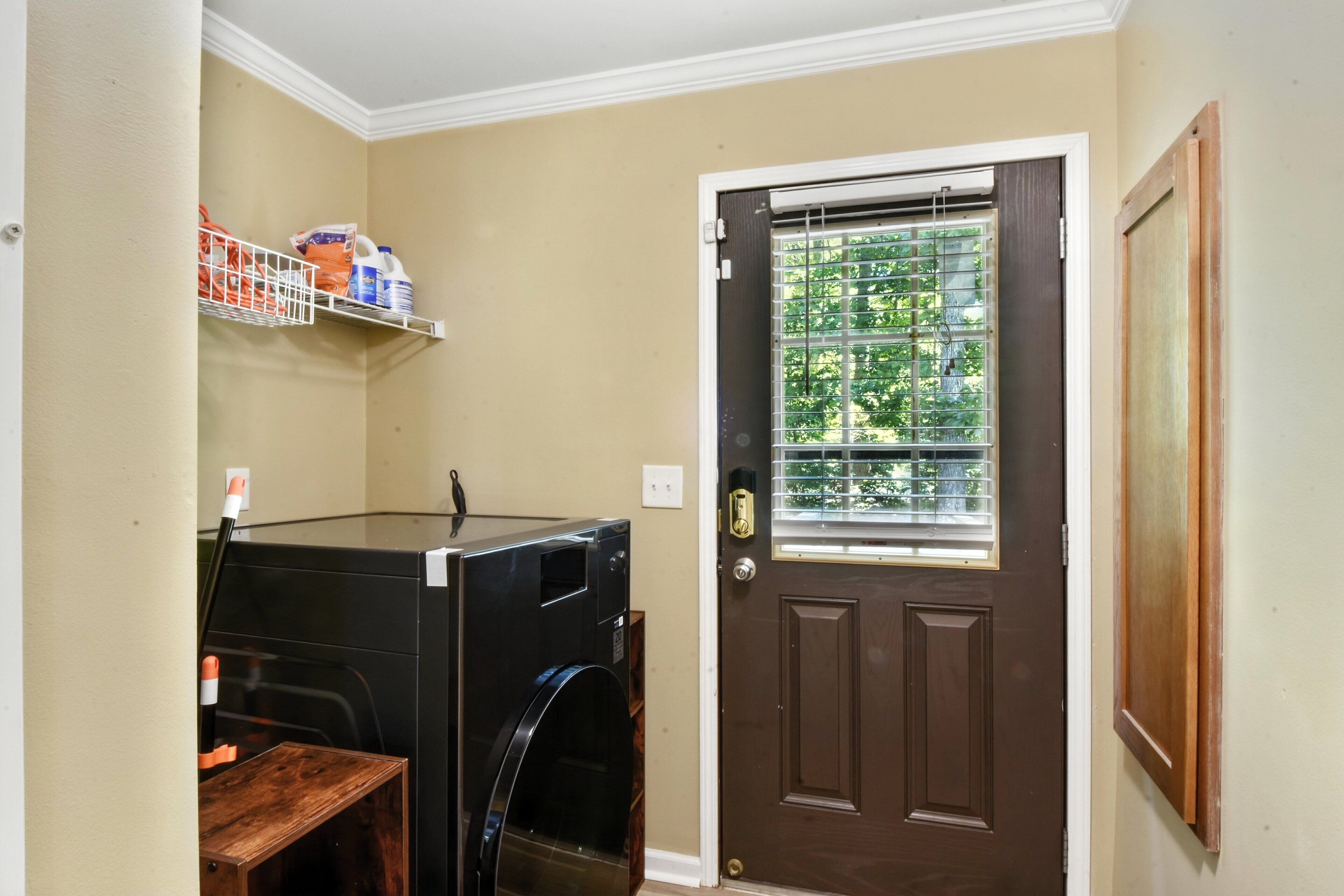 A laundry room with a washing machine, a shelf with cleaning supplies, and a door with a window.