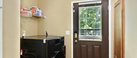 A laundry room with a washing machine, a shelf with cleaning supplies, and a door with a window.